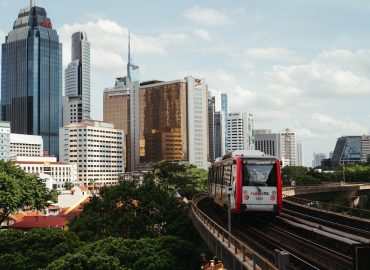 photo-1727271551315-9d61f124460f.jpg Modern MRT train traveling through Kuala Lumpur with city skyline showing Malaysia's infrastructure development. Photo by Unsplash