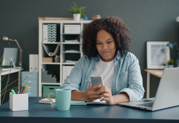 Woman using smartphone and laptop in modern office workspace for daily productivity tasks. Photo by Unsplash.