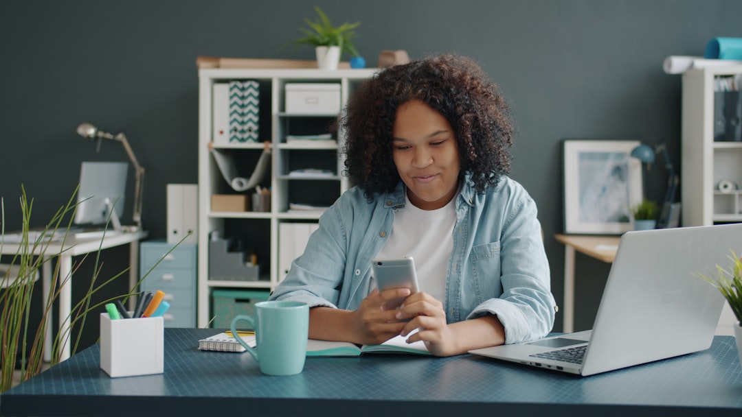 Woman using smartphone and laptop in modern office workspace for daily productivity tasks. Photo by Unsplash.